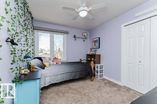 Room featuring a window with roller shade, ceiling fan with integrated lighting, bi-fold closet doors, and plush carpet flooring - 1727 65 Street, Edmonton, AB - Indoor Photo Showing Bedroom