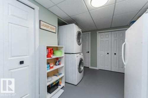 Laundry area featuring a stackable washer and dryer, additional white appliance, paneled doors with black hardware, and a drop-ceiling with recessed lighting - 1727 65 Street, Edmonton, AB - Indoor Photo Showing Laundry Room
