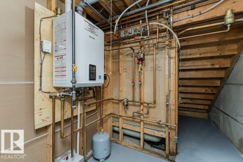 Tankless water heater installation, visible plumbing with copper piping, unfinished wood framing, concrete foundation wall, and painted concrete flooring - 1727 65 Street, Edmonton, AB - Indoor Photo Showing Basement