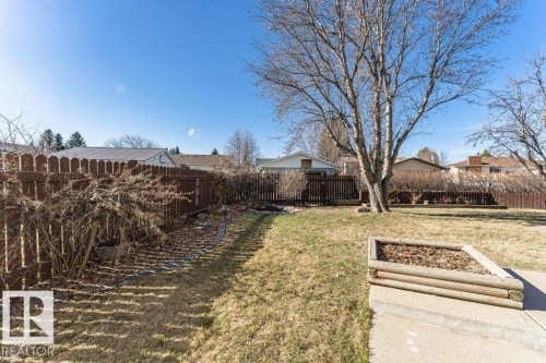 Expansive fenced backyard featuring mature deciduous trees and a raised garden bed with a log-style perimeter - 1727 65 Street, Edmonton, AB - Outdoor
