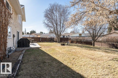 Spacious backyard featuring a concrete patio, mature trees, wood fence, and a stucco exterior - 1727 65 Street, Edmonton, AB - Outdoor