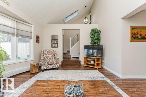 Living area featuring vaulted ceilings, wood-finish flooring, a skylight, and large windows with privacy blinds - 1727 65 Street, Edmonton, AB - Indoor
