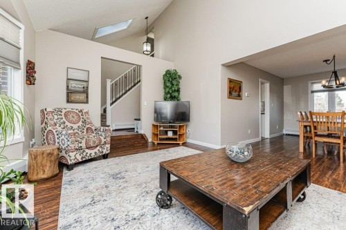 Living area featuring wood-finish flooring, a vaulted ceiling with a skylight, and an open entryway to the dining space - 1727 65 Street, Edmonton, AB - Indoor Photo Showing Living Room