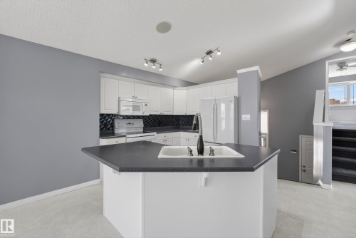 Kitchen featuring white cabinetry, dark countertops, a central island with an integrated sink, a dark tile backsplash, and recessed lighting - 720 87 Street, Edmonton, AB - Indoor Photo Showing Kitchen