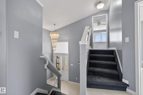 Multi-level entryway featuring a tiered chandelier, double entry doors with decorative glass, and a carpeted staircase with white railings - 720 87 Street, Edmonton, AB - Indoor Photo Showing Other Room