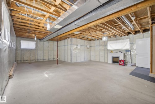Spacious unfinished basement featuring exposed ceiling joists, concrete flooring, and a built-in fireplace with a white mantel - 720 87 Street, Edmonton, AB - Indoor Photo Showing Basement