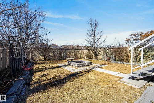 Expansive backyard featuring a stone-lined fire pit, concrete paver pathways, a tiered landscape, a wooden perimeter fence, and mature trees - 720 87 Street, Edmonton, AB - Outdoor With View