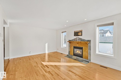 Living area featuring hardwood floors, a stone-clad fireplace with a wooden mantel, and two windows - 10823 130 Street, Edmonton, AB - Indoor Photo Showing Living Room With Fireplace