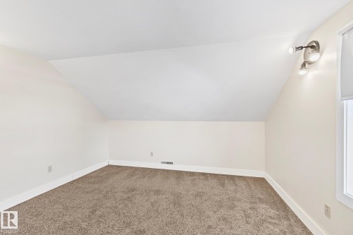 This room features a neutral color palette, textured carpet flooring, and a window with a roller blind - 10823 130 Street, Edmonton, AB - Indoor Photo Showing Other Room