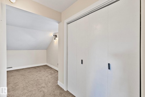 This room features plush carpeted flooring, a wall-mounted light fixture, and white bi-fold closet doors with black hardware - 10823 130 Street, Edmonton, AB - Indoor Photo Showing Other Room