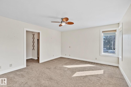 This spacious room features neutral-toned carpet, a ceiling fan with light, and a window providing natural light - 10823 130 Street, Edmonton, AB - Indoor Photo Showing Other Room
