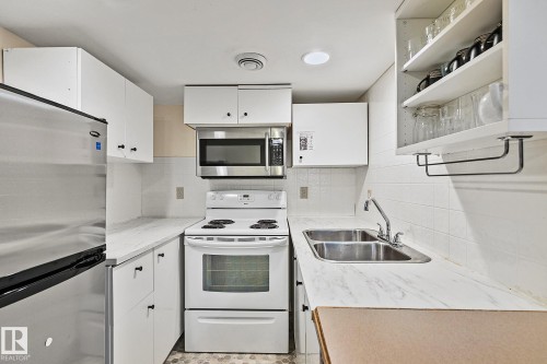 The kitchen features white cabinetry, a double basin stainless steel sink, a stainless steel refrigerator, and an electric range with an overhead microwave - 10823 130 Street, Edmonton, AB - Indoor Photo Showing Kitchen With Double Sink