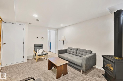 Living area featuring carpet flooring, recessed lighting, and a freestanding fireplace with a visible flue - 10823 130 Street, Edmonton, AB - Indoor
