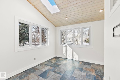This bright room features a vaulted wood-paneled ceiling with a skylight, slate tile flooring, and two large windows providing ample natural light - 10823 130 Street, Edmonton, AB - Indoor Photo Showing Other Room