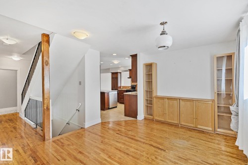 The property features hardwood floors, a staircase with dark banisters, and built-in cabinetry with glass-fronted shelves - 10823 130 Street, Edmonton, AB - Indoor Photo Showing Other Room