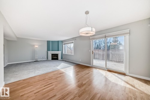 Bright living space featuring wood-finish flooring, a contemporary ceiling light fixture, and a sliding glass door leading to an exterior deck - 2709 124 Street, Edmonton, AB - Indoor Photo Showing Other Room With Fireplace