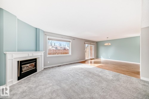 Spacious living area featuring a white fireplace with a black insert, light blue accent walls, and a large window - 2709 124 Street, Edmonton, AB - Indoor With Fireplace