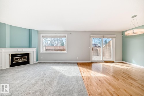 Living area featuring a white mantel fireplace, a window overlooking exterior foliage, and a sliding glass door providing access to a deck - 2709 124 Street, Edmonton, AB - Indoor Photo Showing Living Room With Fireplace