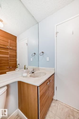 Bathroom vanity with a light-colored countertop and integrated sink, accompanied by wood-finish cabinetry - 2709 124 Street, Edmonton, AB - Indoor Photo Showing Bathroom