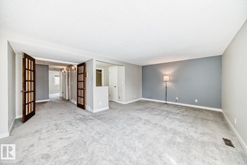 Spacious interior room featuring light gray carpeting, neutral wall colors, a distinct accent wall, white baseboards, and double French doors with frosted glass panels - 2709 124 Street, Edmonton, AB - Indoor Photo Showing Other Room