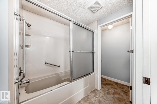 Bathtub and shower combination featuring a white surround, sliding frosted glass doors, and a chrome shower fixture - 2709 124 Street, Edmonton, AB - Indoor