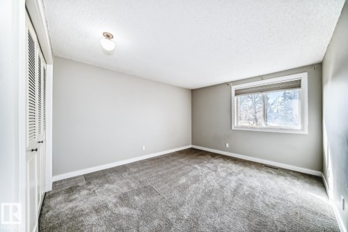 Neutral gray walls complement the gray carpeting in this room featuring a window with a roller shade, louvered bi-fold closet doors, and a ceiling-mounted light fixture - 2709 124 Street, Edmonton, AB - Indoor Photo Showing Other Room