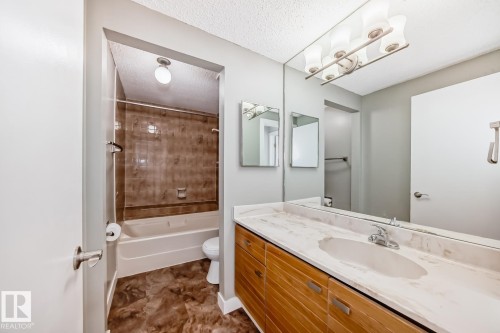 Bathroom featuring a wide vanity with a stone-finish countertop, an integrated sink, and an expansive mirror - 2709 124 Street, Edmonton, AB - Indoor Photo Showing Bathroom