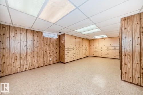 Room featuring extensive built-in cabinetry with multiple drawers and upper cupboards, wood-paneled walls, and a suspended ceiling with integrated lighting - 2709 124 Street, Edmonton, AB - Indoor