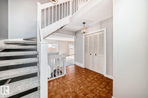 Entryway featuring terra cotta style tile flooring, a carpeted spiral staircase with white railings, a bi-fold louvered closet, and a contemporary pendant light fixture - 2709 124 Street, Edmonton, AB - Indoor Photo Showing Other Room