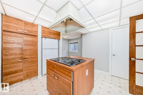 Functional kitchen featuring extensive wood-finish cabinetry, a central island with a built-in cooktop, a white refrigerator, and a suspended range hood - 2709 124 Street, Edmonton, AB - Indoor