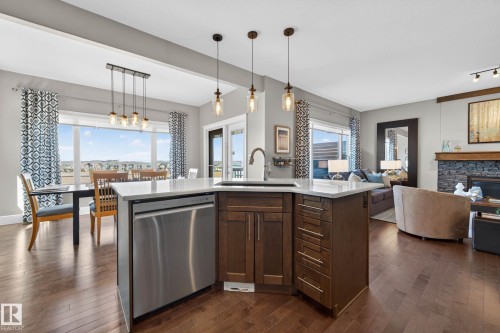 Open-concept kitchen featuring an island with a stainless steel dishwasher, a quartz countertop, and pendant lighting - 2086 Redtail Common, Edmonton, AB - Indoor Photo Showing Kitchen With Fireplace With Upgraded Kitchen