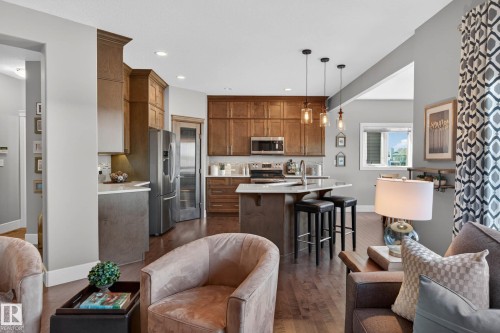 Open-concept kitchen featuring wood-finish flooring, custom cabinetry, stainless steel appliances, a center island with seating, and pendant lighting - 2086 Redtail Common, Edmonton, AB - Indoor