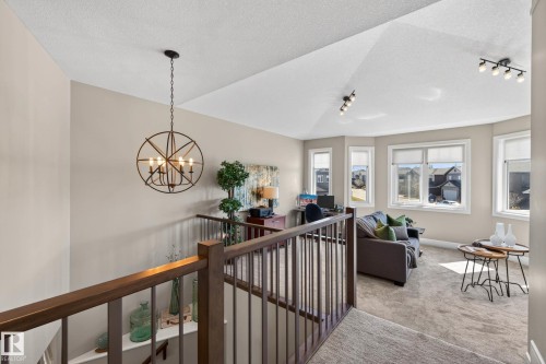 Open landing area featuring a modern chandelier, wood-finish railing, bay windows, textured carpet, and track lighting - 2086 Redtail Common, Edmonton, AB - Indoor Photo Showing Other Room
