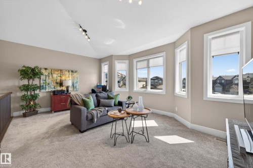 Carpeted loft space featuring multiple windows, sloped ceiling with track lighting, and a dark wood-finish railing - 2086 Redtail Common, Edmonton, AB - Indoor Photo Showing Living Room