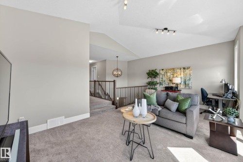 Carpeted living area featuring a vaulted ceiling with track lighting, a railing overlooking a lower level, and light gray wall paint - 2086 Redtail Common, Edmonton, AB - Indoor Photo Showing Living Room