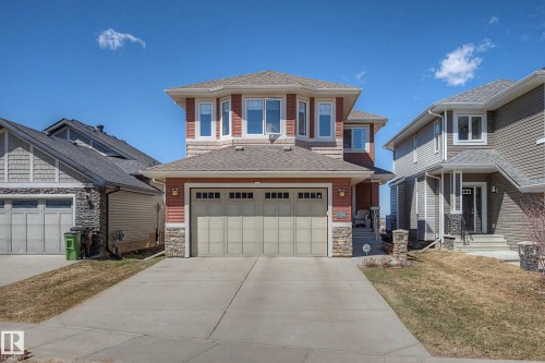 Two-story residence featuring a two-car garage with panel detailing, stone facade accents, and red siding - 2086 Redtail Common, Edmonton, AB - Outdoor With Facade