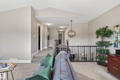Open loft area featuring vaulted ceilings, plush carpeting, an iron spindle railing, and a modern spherical chandelier - 2086 Redtail Common, Edmonton, AB - Indoor Photo Showing Other Room