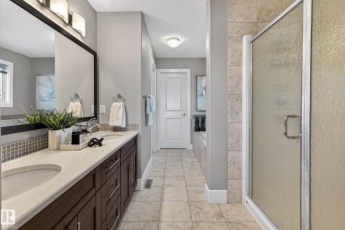 Bathroom featuring a dual vanity with a light-toned countertop, dark wood cabinetry, and a textured tile backsplash - 2086 Redtail Common, Edmonton, AB - Indoor Photo Showing Bathroom
