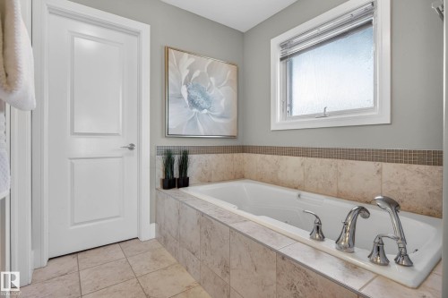 Built-in soaking tub with chrome fixtures, surrounded by large format tile and a glass mosaic accent border - 2086 Redtail Common, Edmonton, AB - Indoor Photo Showing Bathroom