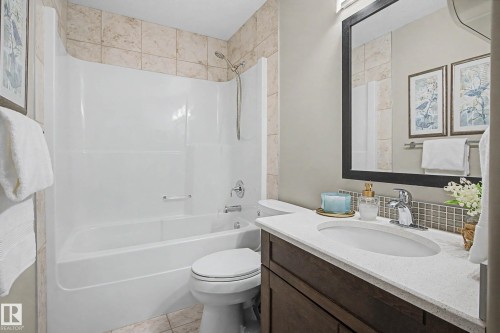 Bathroom featuring a white tub/shower combination, light-toned tile surround, dark wood-finish vanity with an integrated sink, and a light-colored countertop - 2086 Redtail Common, Edmonton, AB - Indoor Photo Showing Bathroom