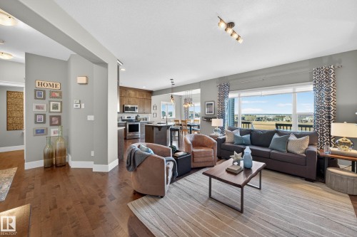 Spacious open-concept living area featuring wood-finish flooring, a large picture window, recessed lighting, and an expansive kitchen with built-in cabinetry and stainless steel appliances - 2086 Redtail Common, Edmonton, AB - Indoor Photo Showing Living Room