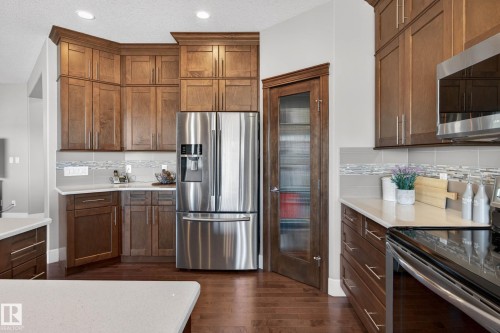 Gourmet kitchen featuring a stainless steel refrigerator, abundant wood cabinetry, quartz countertops, a decorative tile backsplash, and wood-finish flooring - 2086 Redtail Common, Edmonton, AB - Indoor Photo Showing Kitchen With Upgraded Kitchen
