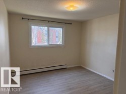 This room features light-colored walls, wood-look flooring, and a window with a view of trees and a building - 