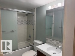Bathroom with a vanity featuring a white sink, a mirror with integrated lighting, and a bathtub with a shower and frosted glass sliding doors - 