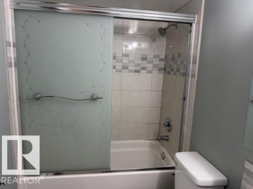 Bathroom featuring a tub and shower combination with sliding glass doors, and tiled walls - 201 10811 115 Street, Edmonton, AB - Indoor Photo Showing Bathroom
