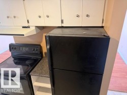 Kitchen area featuring a black electric range, a black refrigerator, and white upper cabinetry - 