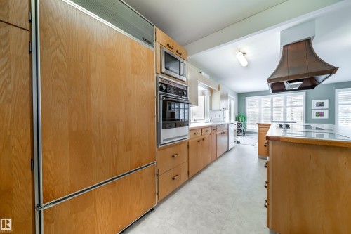 Kitchen featuring wood cabinetry, integrated panel refrigerator, built-in oven and microwave, central island with cooktop, and a copper-toned range hood - 10231 46 Street, Edmonton, AB - Indoor Photo Showing Kitchen