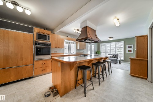 Spacious kitchen featuring light wood cabinetry, integrated refrigerator, built-in oven and microwave, an expansive island with a cooktop, and a distinctive copper range hood - 10231 46 Street, Edmonton, AB - Indoor Photo Showing Kitchen