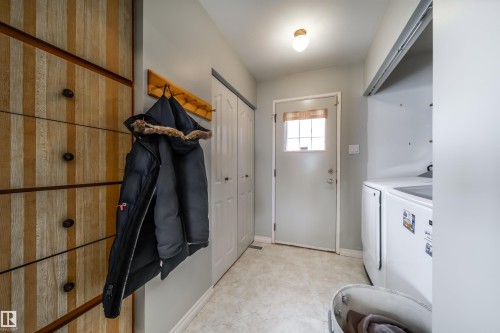 Entry area featuring a built-in wood-finish storage unit with dark hardware, a light-colored entry door with window, and a wall-mounted coat rack - 10231 46 Street, Edmonton, AB - Indoor Photo Showing Other Room