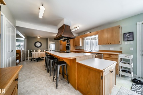 Kitchen featuring light wood cabinetry, white countertops, built-in wall oven, and a copper-toned range hood over a central island with seating - 10231 46 Street, Edmonton, AB - Indoor Photo Showing Kitchen With Double Sink